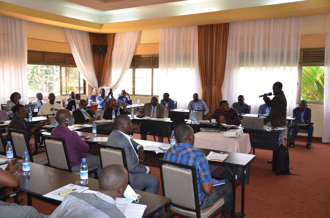 Participants seated in a conference room during a findings dissemination workshop, one participant speaking into a microphone