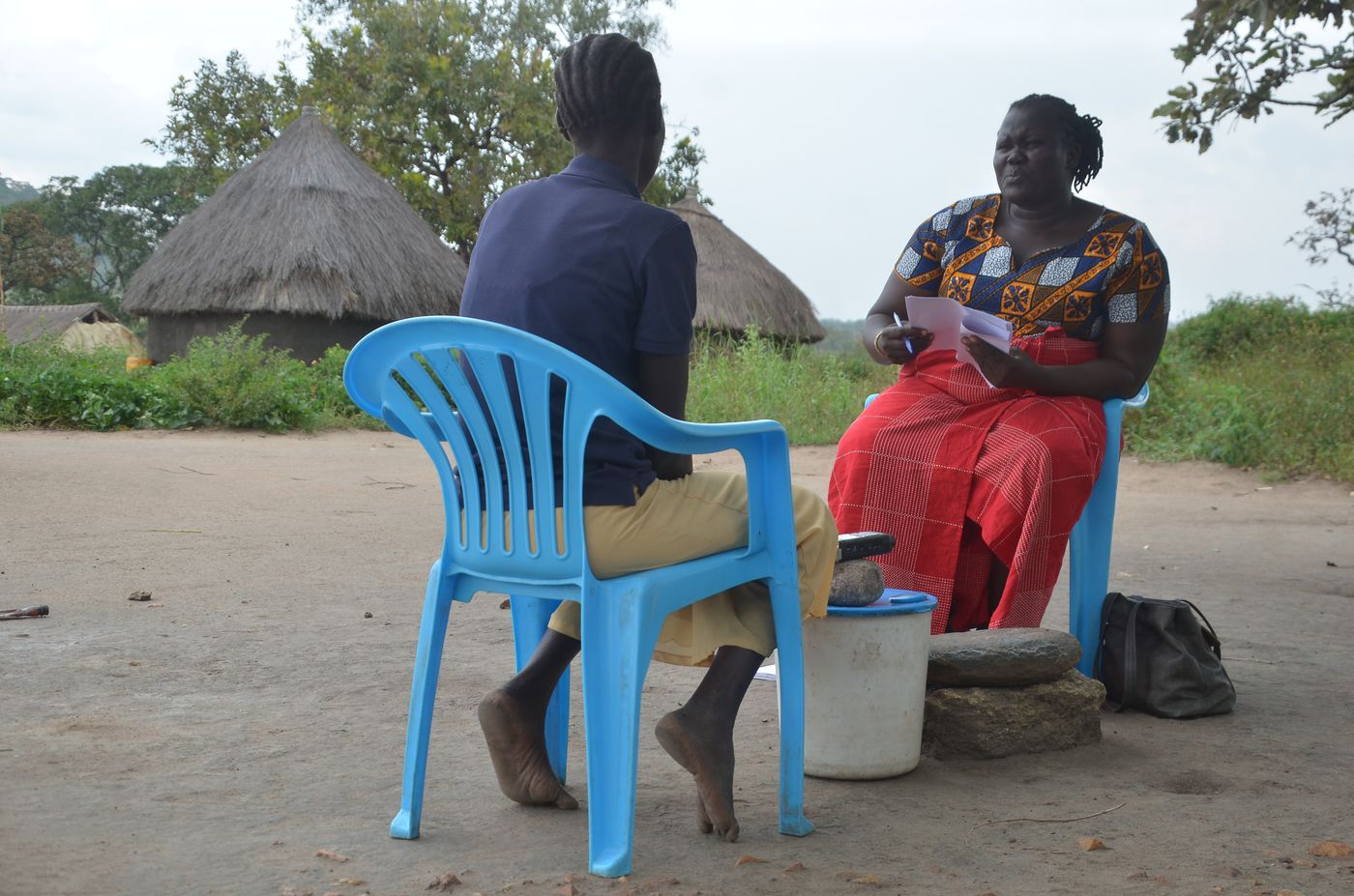 A NATE Africa researcher conducting a one-to-one interview with a community member outside thatched homesteads